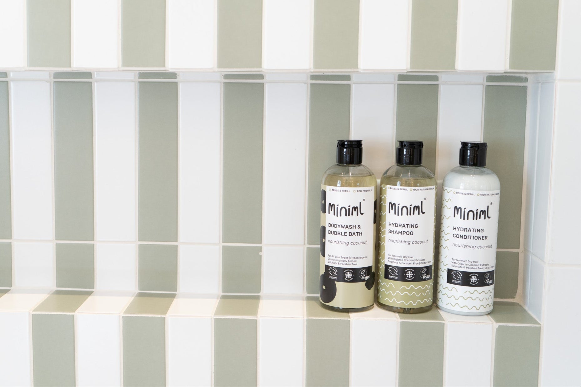 Three bottles of 'Minimal' skincare products on a tiled shelf with striped tiles.